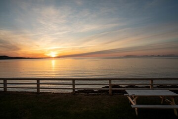 Fototapeta premium Wooden table and bench situated on a beach with a beautiful orange and pink sky in the background