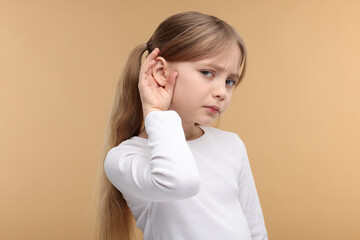 Little girl with hearing problem on pale brown background