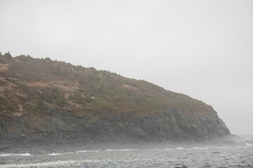 Scenic view of sea waves crashing against rocky cliffs on a stormy day in Newfoundland, Canada