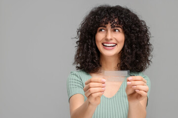 Young woman holding teeth whitening strips on grey background, space for text - obrazy, fototapety, plakaty