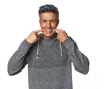 Middle-aged Latino man smiles, pointing fingers at mouth.