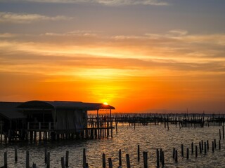 Fototapeta premium Aerial view of a bright sunset sky over wooden poles in the clear Songkhla Lake,Thailand