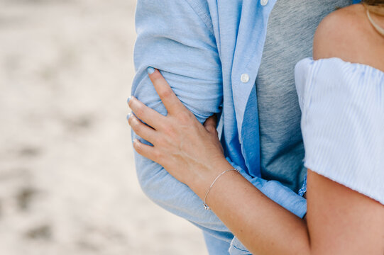 Female and male hug on beach ocean and enjoy sunny summer day. Man and woman embrace on sand sea. Romantic couple in love hugging on seashore. Spending time together. Closeup of hands. Back view