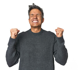 Middle-aged Latino man celebrating a victory, passion and enthusiasm, happy expression.