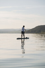 A man is standing and paddling on a paddleboard on the water. Enjoying the vacation.  Landscape in the background.