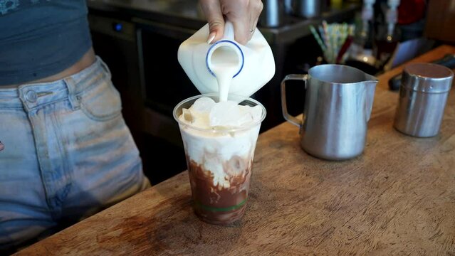 Closeup of barista pouring cup in the glass and making iced latte