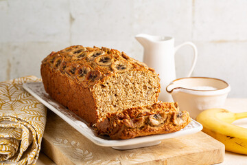 Coconut Flour Banana Bread on a wooden board. Ingredients on the beige table surface.