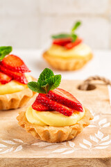 Strawberry tartlets with vanilla pastry cream - mini fruit tarts filled with custard vanilla pastry cream in a cookie crust. Homemade Dessert on awooden board, Vertical image.