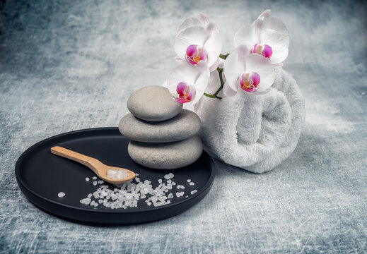 Spa decoration with gorgeous orchid flowers in white and cyclamen, spa stones and rolled towel on textured background