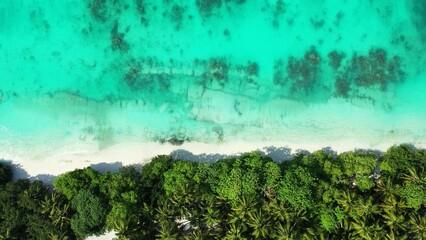 Aerial drone shot of the ocean washing the beach of a small island with palm trees in Southeast Asia