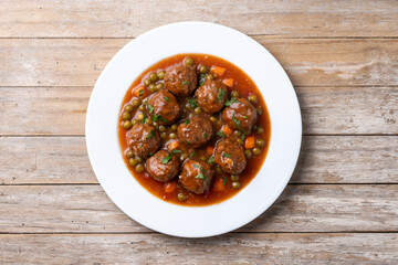 Meatballs, green peas and carrot with tomato sauce on wooden table. Top view