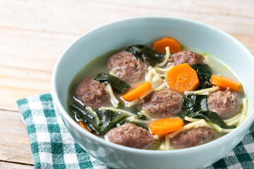 Italian Wedding Soup with meatballs and spinach on wooden table. Close up