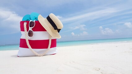 Closeup shot of beach bag with slippers, hat and sunglasses on the sand beach