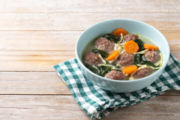 Italian Wedding Soup with meatballs and spinach on wooden table. Copy space