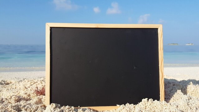 Closeup of a blackboard on a sandy beach against a turquoise sea