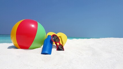 Closeup of a ball, bottle, sunglasses, and flip-flops at a beach on a sunny day