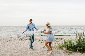 Couple spreading blanket for picnic on sand sea. Happy and funny couple in love on seashore. Female...