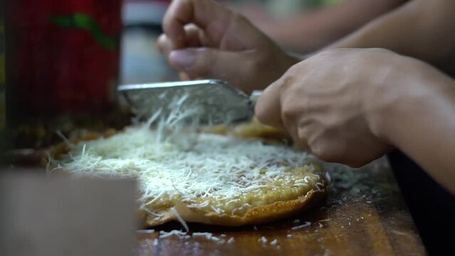 Cianjur, 12 November 2023 - a trader is making sweet martabak. The process of making martabak is by sprinkling cheese and nuts on top of the dough.