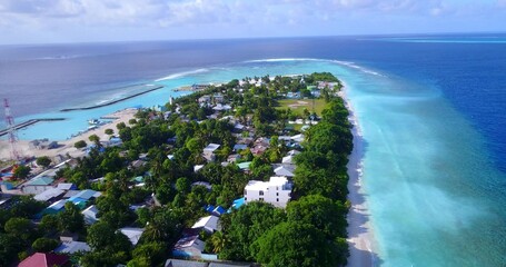 Aerial view of turquoise water by an island with trees and buildings in the Maldives