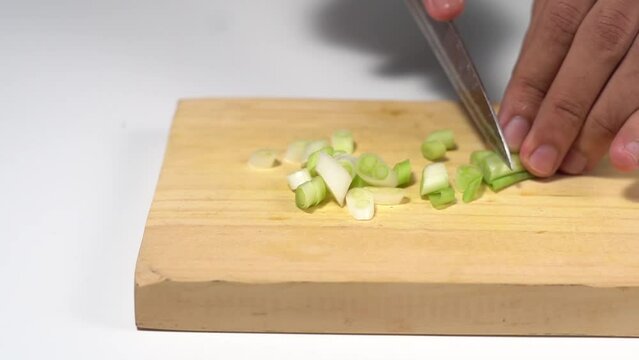 Cutting spring onions close up with knife on wooden cutting board on kitchen table