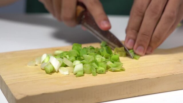 Cutting spring onions close up with knife on wooden cutting board on kitchen table