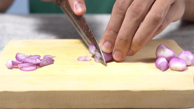 Close-up of male hands cutting fresh shallots on a wooden cutting board on a white background