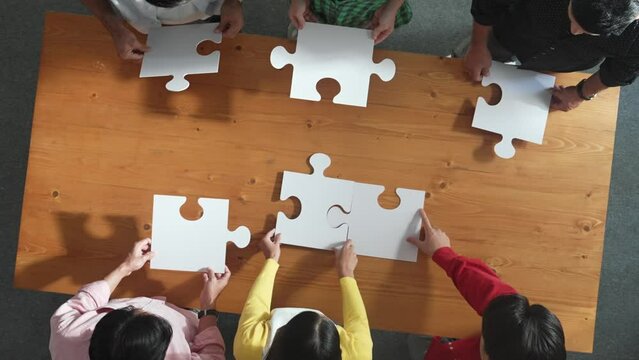Top down view of skilled business people assemble jigsaw puzzle on meeting table. Group of diverse team working together to solve the puzzle. Represented unity, togetherness, cooperative. Convocation.