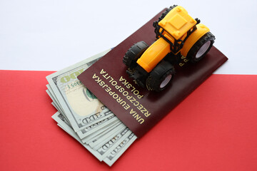 Red polish passport and yellow tractor on US money and smooth red and white flag of Poland close up