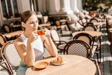 Portrait of happy woman sitting in a cafe outdoor drinking coffee. Woman while relaxing in cafe at table on street, dressed in a white T-shirt and jeans