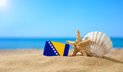 Fototapeta na wymiar Tropical beach with seashells and Bosnia and Herzegovina flag. The concept of a paradise vacation on the beaches of Bosnia and Herzegovina.