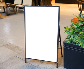 Blank white outdoor advertising stand or sandwich board mock up template. Clear street signage board placed by an outdoor dinning area of a restaurant. Background texture of standee on street. - obrazy, fototapety, plakaty