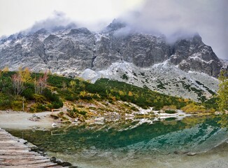 Panoramic photo of the rocky peaks of the High Tatras with the first layer of snow in early autumn above a clear turquoise glacial lake