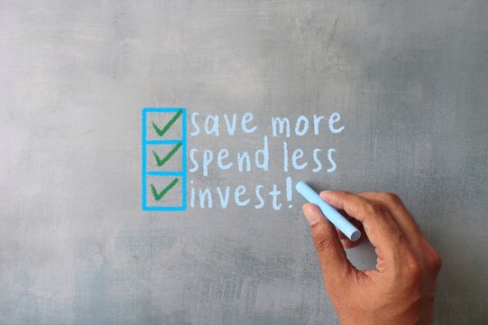 Hand writing on chalkboard text SAVE MORE, SPEND LESS, INVEST. Financial concept.
