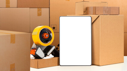 Cardboard boxes for moving. Electronic tablet with blank screen. Tape dispenser. Parcels on table....