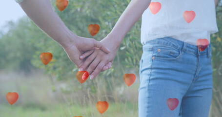Image of red heart balloons floating over mid section of couple in love holding hands in summer - obrazy, fototapety, plakaty