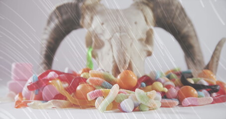 Light trails over halloween candies and goat horns and skull against white background
