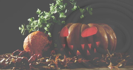 Image of glowing halloween pumpkin, with plant and autumn leaves, on black background - Powered by Adobe