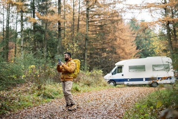 Man with Backpack Using Smartphone by Camper in Autumn Woods