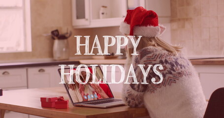 Image of happy holidays text over happy caucasian woman in santa hat on laptop image call - Powered by Adobe