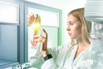 Woman microbiologist. Girl with laboratory flask in her hands. Scientist is standing in laboratory. Microbiologist at work. Young woman in medical laboratory. Microbiologist near scientific equipment