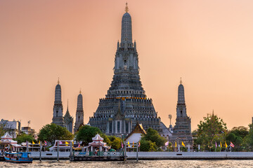 Wat Arun stupa, a significant landmark of Bangkok, Thailand, stands prominently along the Chao Phraya River, with a beautiful sunset sky.