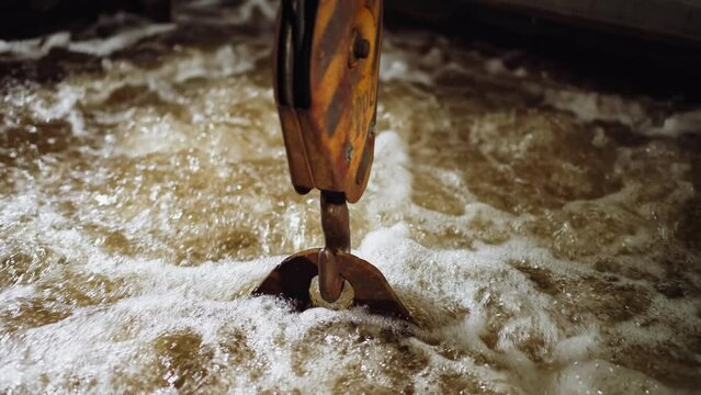 Crane hook submerging into foamy water in a dynamic industrial metal quenching process