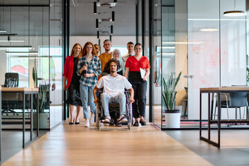 A diverse group of young business people walking a corridor in the glass-enclosed office of a modern startup, including a person in a wheelchair and a woman wearing a hijab - obrazy, fototapety, plakaty