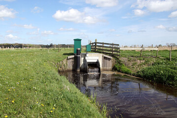 Fototapeta premium Small Dutch tilting weir (kantelstuw) in a ditch. Running water. It regulates the water drainage capacity of the surface water body. Meadows, Spring, April. Netherlands.