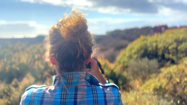 Back view of a woman photographer taking picture outdoor at amazing scenic background in the nature. Traveler take photo of panorama. 4k cinematic footage of tourist enjoying travel alone lifestyle