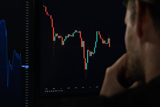 crypto currency investor analyzing digital candle stick chart data on computer screen. stock market broker looking at exchange trading platform indexes. over shoulder view