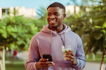 Handsome smiling African American young man holding lemonade drink and mobile phone