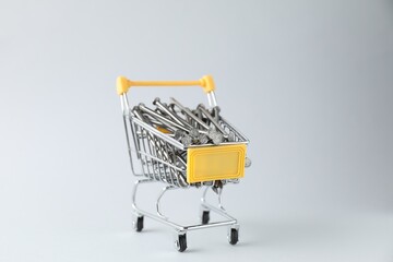 Metal nails in shopping cart on light grey background, closeup