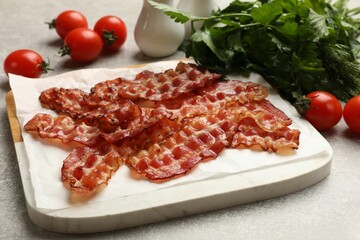Fried bacon slices, tomato and parsley on grey textured table, closeup