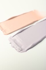 Strokes of pink and purple color correcting concealers on white background